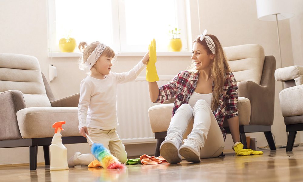 Blog - Woman High Fiving Her Toddler Daughter While They Both are Cleaning the Living Room with Cleaning Supplies on the Floor around them as they Sit